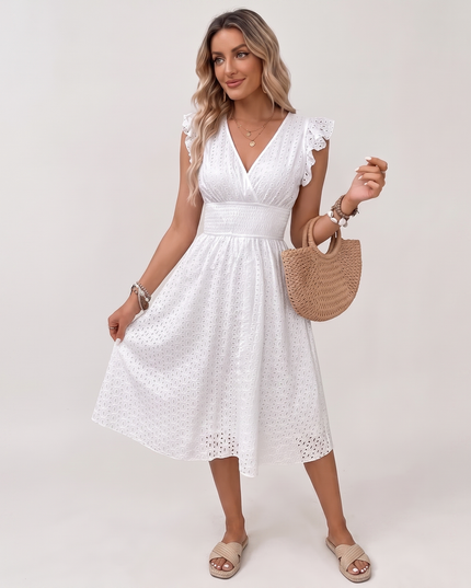 A woman modeling a white sleeveless midi dress with ruffled shoulders and eyelet lace trim, styled with a woven straw handbag and beige slide sandals against a light gray studio background.